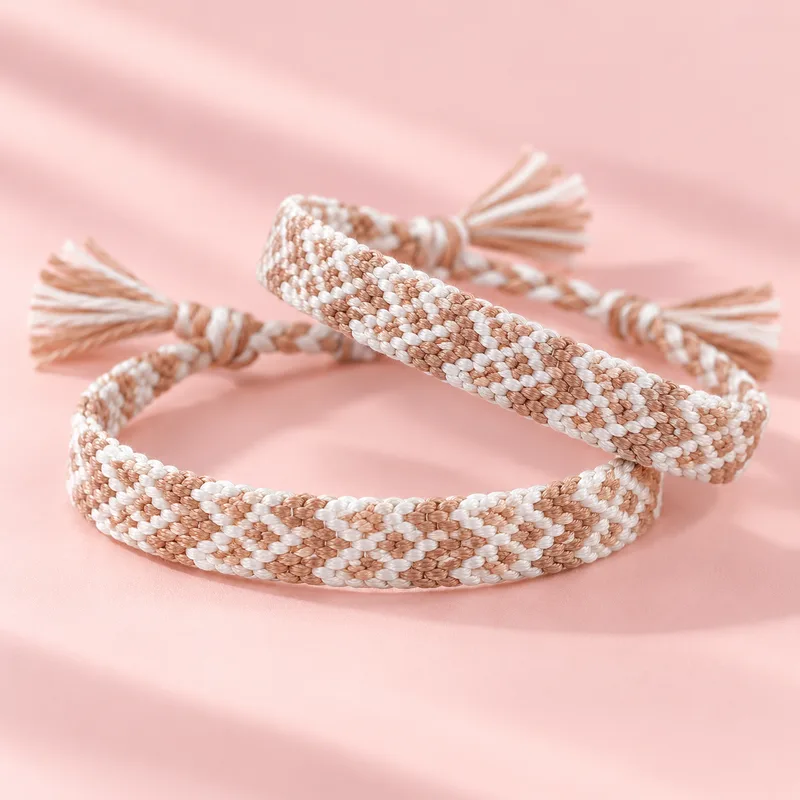 Deux bracelets brésiliens assortis, beige et crème, posés l'un sur l'autre sur fond rose
